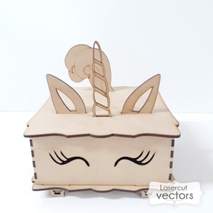 May include: A wooden box shaped like a unicorn's head with a horn, ears, and eyelashes. The box is made of light brown wood and has a white background.