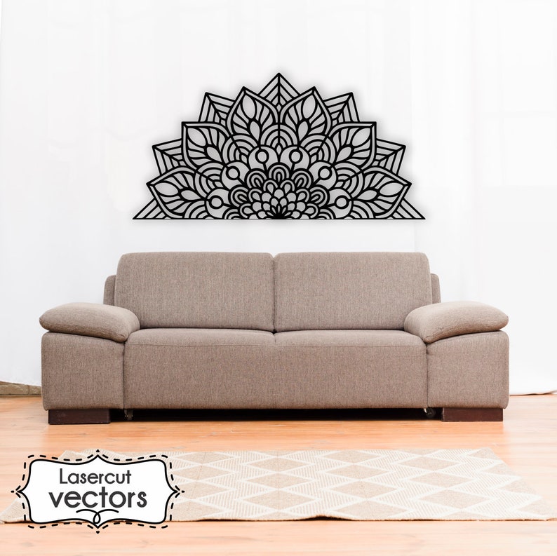 May include: A black and white mandala design in the shape of a half circle, mounted on a white wall above a brown couch. The couch is in front of a white rug with a geometric pattern.