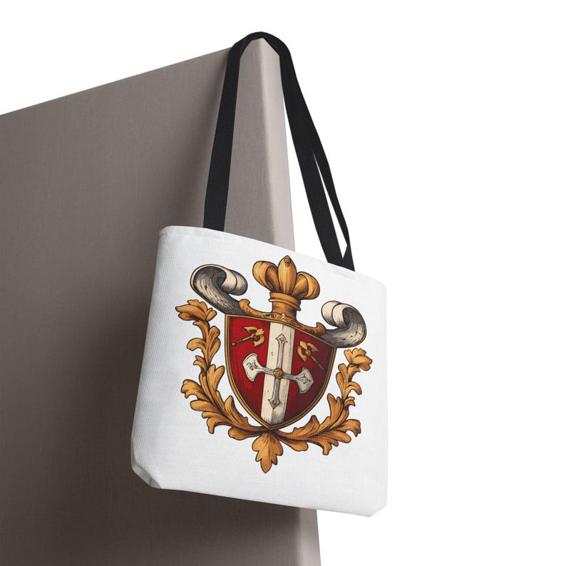May include: White tote bag featuring a detailed heraldic crest design. The crest includes a red and white shield with a cross, a gold crown, and ornate gold leaf accents. The bag has black handles.