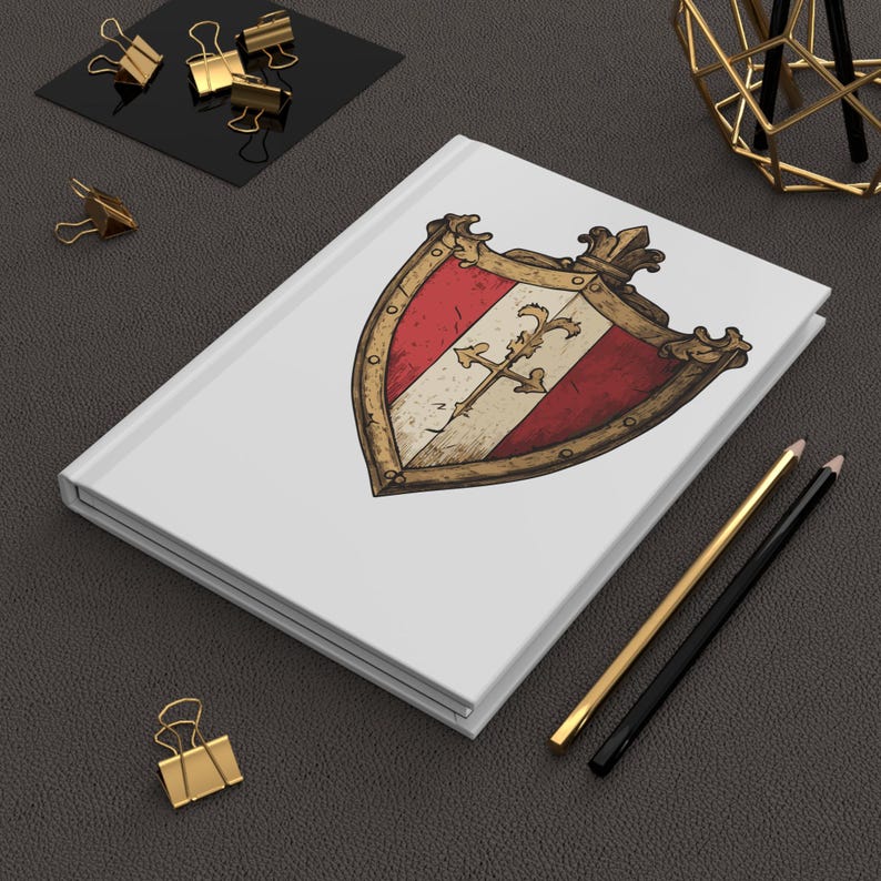 May include: A white journal with a shield design featuring red and white stripes, a gold cross, and a gold border. Gold binder clips, pencils, and a geometric object are also present.
