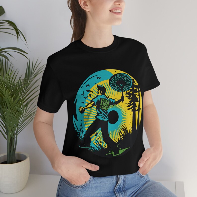 May include: Black t-shirt with a graphic of a person throwing a disc in a forest setting. The graphic includes the text "ESA" and "JUJU".