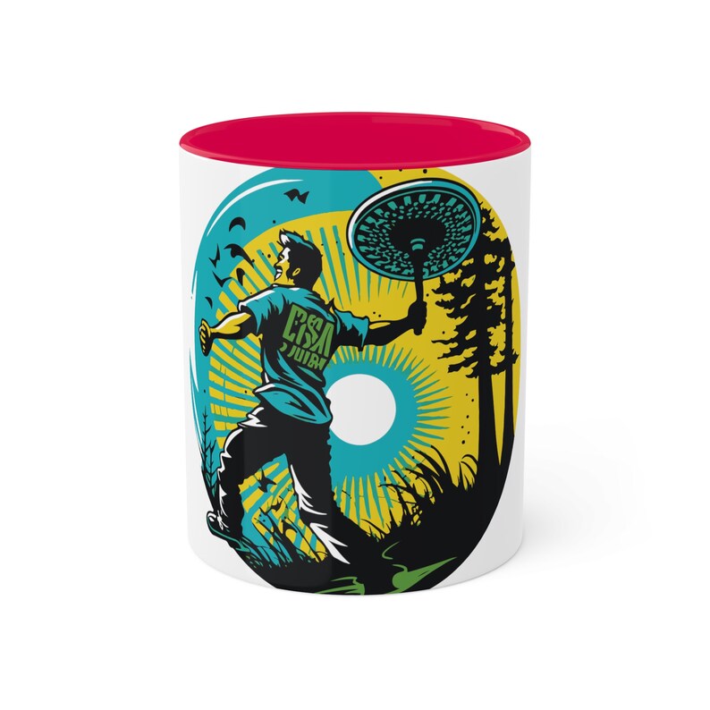 May include: White ceramic mug with a red interior. The mug features a colorful illustration of a person holding a disc in a forest setting. The text "CSA JUIN" is on the person's shirt.