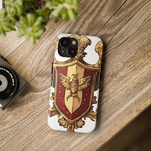 May include: A white phone case featuring a detailed heraldic crest design. The crest is primarily gold, red, and white, with a central eagle emblem. The case has a glossy finish and is designed to fit a smartphone.