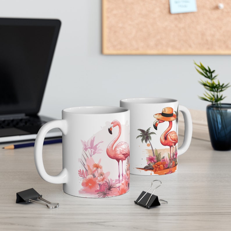 May include: Two white ceramic mugs with flamingo designs. One mug features a flamingo wearing a straw hat and palm trees, while the other mug features a flamingo with pink flowers and leaves.