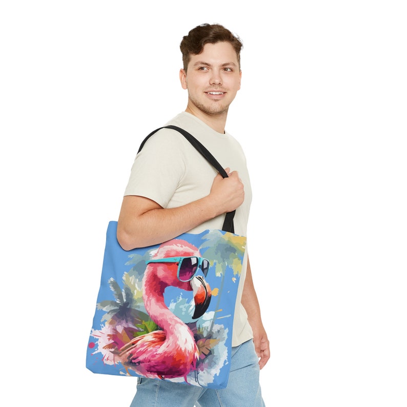 May include: A blue tote bag with a pink flamingo wearing sunglasses and a palm tree design. The bag has black straps.