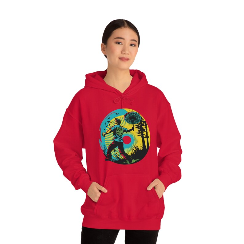 May include: Red hooded sweatshirt with a graphic print of a person throwing a disc in a forest setting. The graphic is in a retro style with a yellow, blue, and green color scheme.