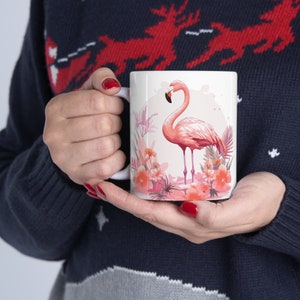 May include: White ceramic mug with a pink flamingo standing in a bed of pink flowers. The mug has a watercolor-style design.