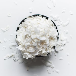 May include: A black bowl filled with white coconut flakes, with additional flakes scattered around the bowl on a white surface.