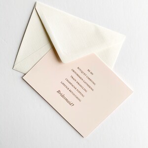 Puede incluir: Una tarjeta rosa con el texto "Be My Bridesmaid?" y una lista de tareas: "Bouquet Carrying", "Groomsmen Gathering", "Train Wrangling", "Champagne Popping", "Lipstick Retouching".