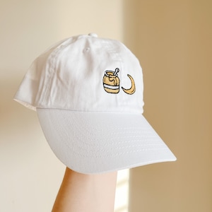 May include: White baseball cap with an embroidered design of a jar of honey and a crescent moon.