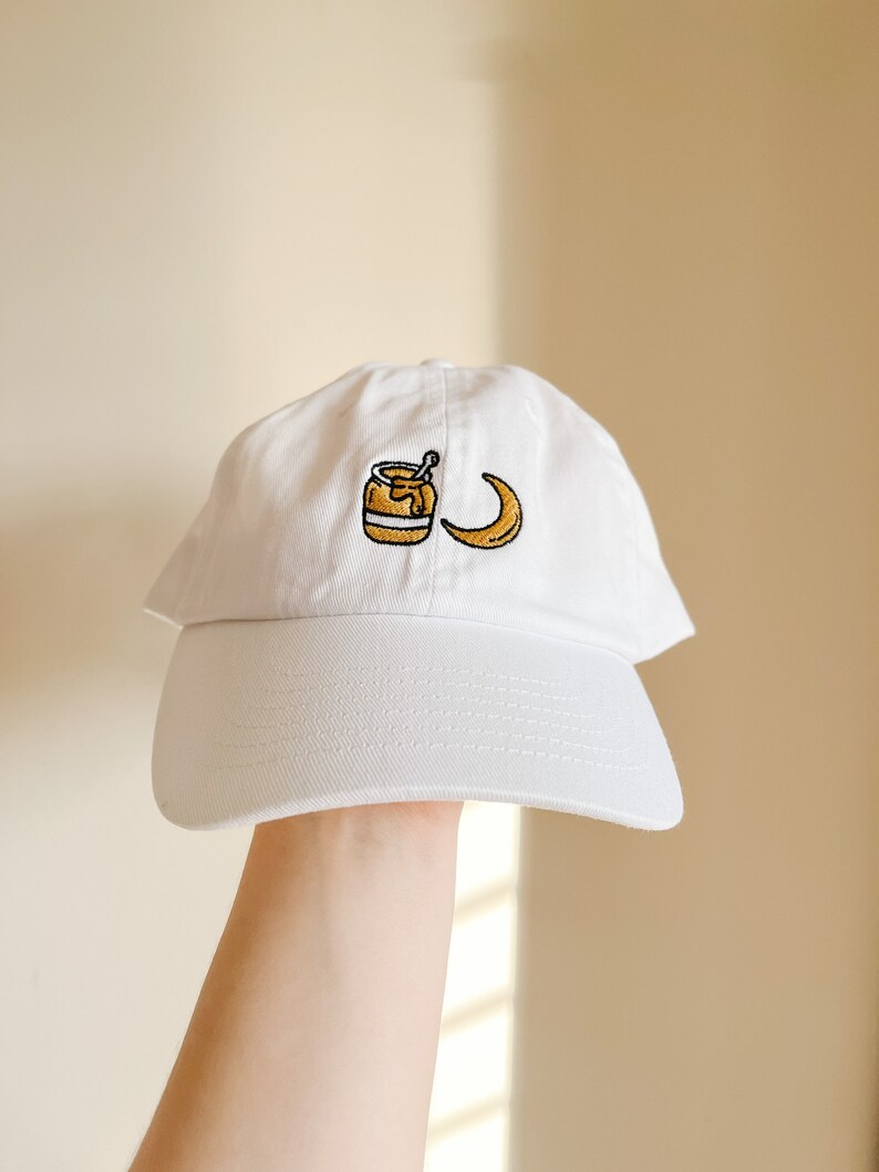 May include: White baseball cap with an embroidered design of a jar of honey and a crescent moon.