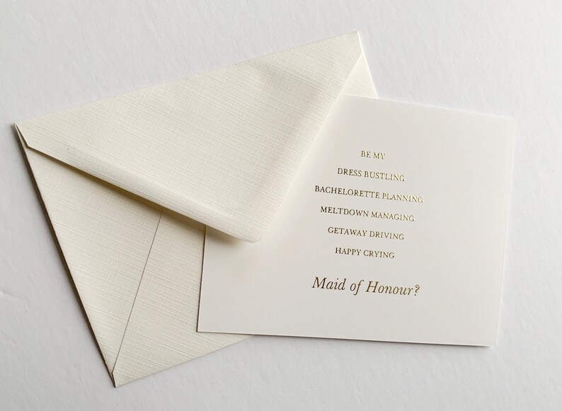 Puede incluir: Una tarjeta blanca con letras doradas que dice "Be my Dress Bustling, Bachelorette Planning, Meltdown Managing, Getaway Driving, Happy Crying, Maid of Honour?"