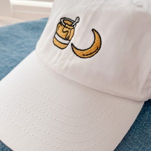 May include: White baseball cap with an embroidered design of a jar of honey and a crescent moon.