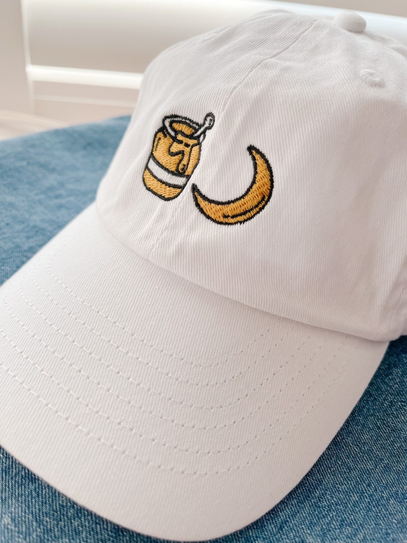 May include: White baseball cap with an embroidered design of a jar of honey and a crescent moon.