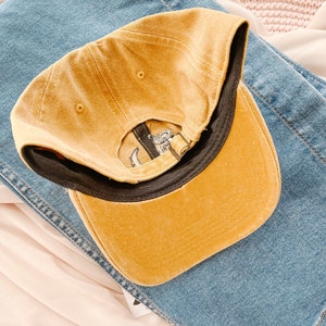 May include: A mustard yellow baseball cap with a black brim. The cap is made of a soft, textured fabric.