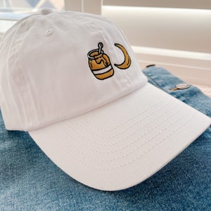 May include: White baseball cap with an embroidered design of a jar of honey and a crescent moon.