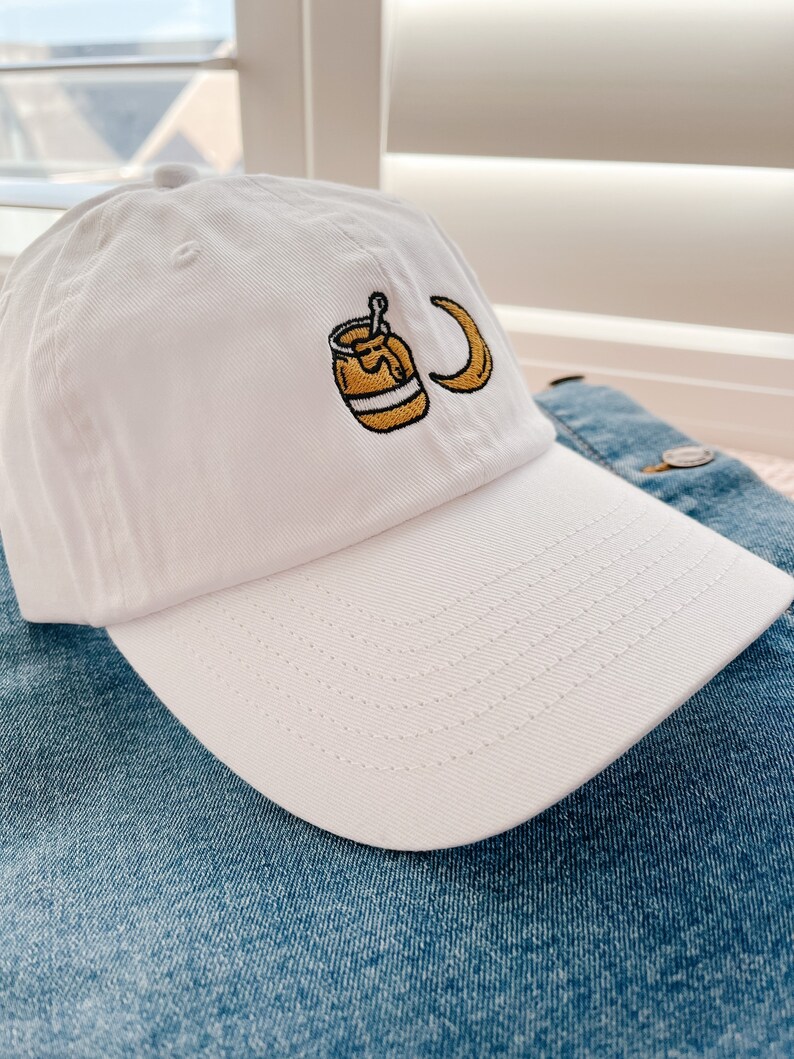 May include: White baseball cap with an embroidered design of a jar of honey and a crescent moon.