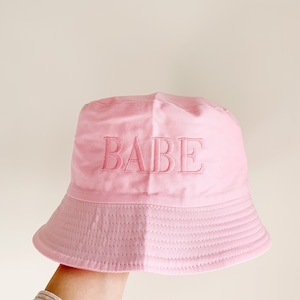 May include: A pink bucket hat with the word "BABE" embroidered on the front.