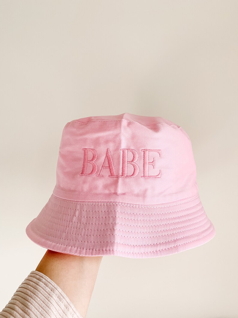May include: A pink bucket hat with the word "BABE" embroidered on the front.