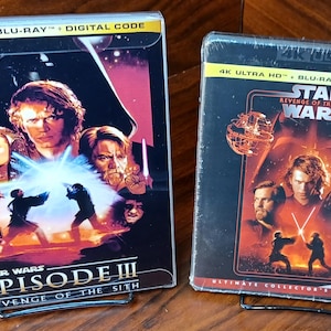 May include: Two Star Wars movie cases. The left case is for Episode III: Revenge of the Sith, featuring a collage of characters and the title. The right case is for Revenge of the Sith, with a red and orange color scheme and character portraits.