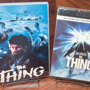 May include: Two Blu-ray disc cases for the movie "The Thing" by John Carpenter. The case on the left features a scene from the movie with a character in a snowy landscape. The case on the right features a close-up of the creature from the movie.
