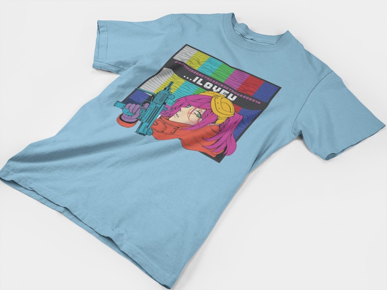 May include: A light blue t-shirt with a graphic print of a woman with pink hair holding a gun. The graphic is set against a colorful background of a television screen with the text "...ILOVEU" in the center.