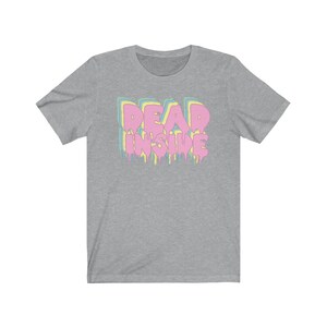 May include: A heather gray t-shirt with the text "DEAD INSIDE" in a dripping, pastel-colored design. The text is layered with pink, yellow, blue, and green colors. The shirt has short sleeves and a crew neck.