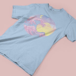 May include: A light blue t-shirt with a pastel pink and yellow graphic of a wave with a crescent moon in the sky.