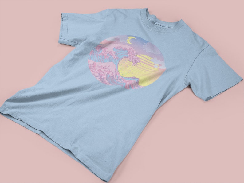 May include: A light blue t-shirt with a pastel pink and yellow graphic of a wave with a crescent moon in the sky.