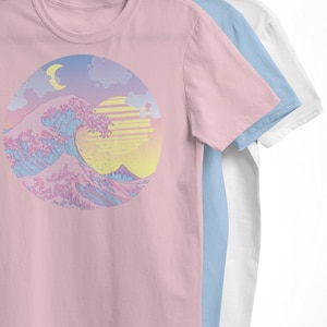 May include: A pink t-shirt with a pastel colored graphic of a wave, a crescent moon, and a sun. The graphic is in a circle.