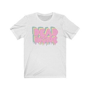 May include: White t-shirt with the text "DEAD INSIDE" in a layered, dripping font. The text features pastel colors: pink, yellow, blue, and green. The shirt is a crew neck style.