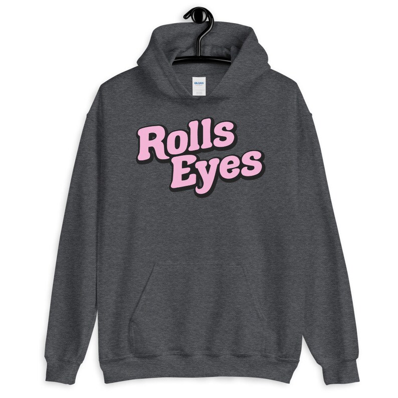 Puede incluir: Una sudadera con capucha gris oscuro con un gr&aacute;fico rosa que dice "Rolls Eyes" en una fuente retro.