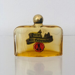 May include: A small amber glass bottle with a gold top. The bottle has a label that reads "Patric.er Alt-Lavendel" and a red seal with a cartoon man wearing a top hat.