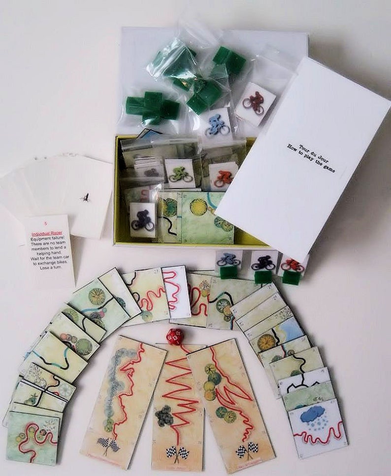 Pu&ograve; includere: Un gioco da tavolo chiamato "Tour du Jour" con biciclette verdi, rosse e blu, un dado e carte da gioco con illustrazioni di strade tortuose. Il gioco include istruzioni su come giocare.