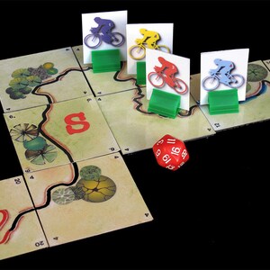 Pu&ograve; includere: Un tabellone da gioco rosso, blu, giallo e verde con quattro pedine da ciclista e un dado rosso con numeri bianchi. Il tabellone ha un percorso tortuoso con una linea rossa e alberi verdi.