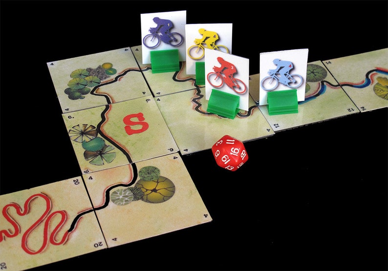 Pu&ograve; includere: Un tabellone da gioco rosso, blu, giallo e verde con quattro pedine da ciclista e un dado rosso con numeri bianchi. Il tabellone ha un percorso tortuoso con una linea rossa e alberi verdi.