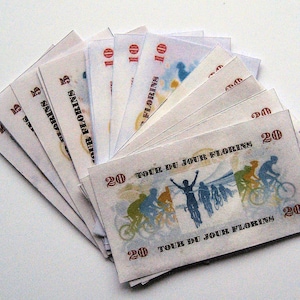 Pu&ograve; includere: Un mazzo di banconote con un tema ciclistico. Le banconote sono stampate con le parole "Tour du Jour Florins" e presentano un disegno di ciclisti che pedalano su una strada. Le banconote sono in tagli da 5, 10 e 20.