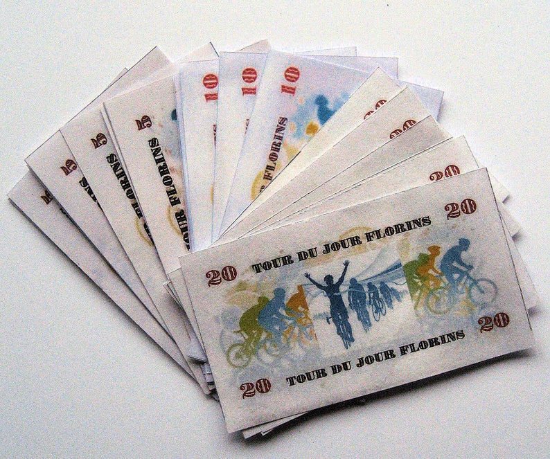 Pu&ograve; includere: Un mazzo di banconote con un tema ciclistico. Le banconote sono stampate con le parole "Tour du Jour Florins" e presentano un disegno di ciclisti che pedalano su una strada. Le banconote sono in tagli da 5, 10 e 20.