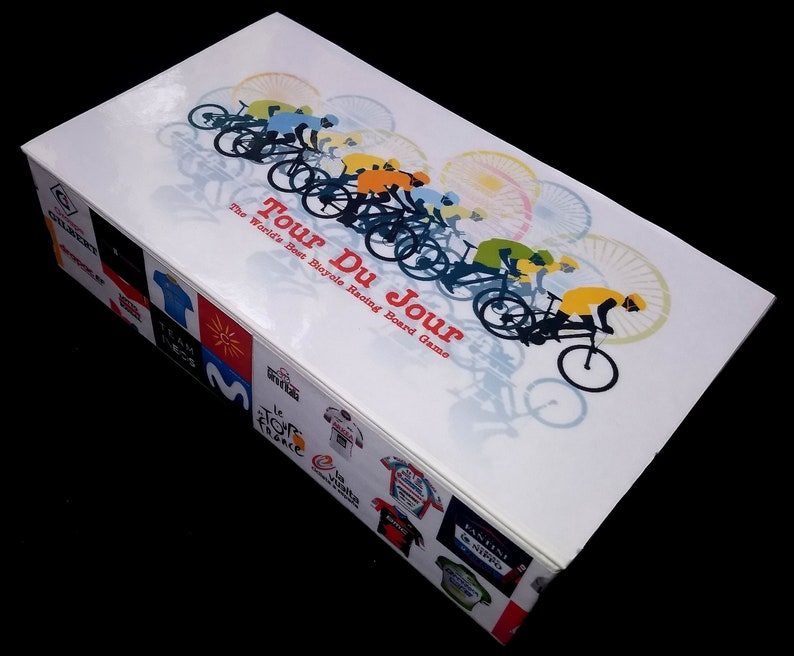Pu&ograve; includere: Una scatola bianca con un'illustrazione colorata di ciclisti che corrono in bicicletta. La scatola &egrave; per un gioco da tavolo chiamato "Tour Du Jour: The World's Best Bicycle Racing Board Game".