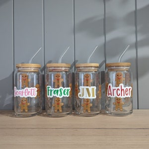 May include: Four clear glass jars with bamboo lids and clear straws. Each jar has a gingerbread man sticker with a name on it: Scarlett, Fraser, JM, and Archer.