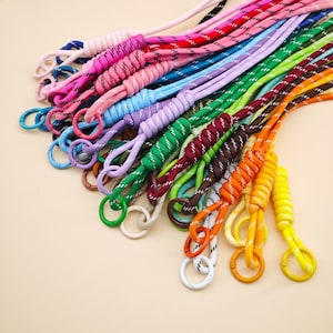 May include: A collection of multi-coloured nylon paracord lanyards, each featuring a tightly wrapped knot section and a circular metal ring clasp. The cords are available in various solid colours and patterned designs including pink, blue, green, orange, yellow, and purple.