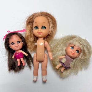 May include: Three vintage dolls with rooted hair and painted facial features. One doll has brown hair and a pink dress, another has blonde hair and a purple dress, and the third doll has a nude body and blonde hair.