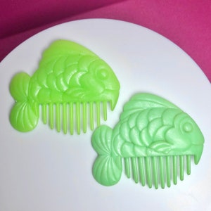 May include: Two green plastic fish-shaped hair combs. The combs have a detailed fish design and are perfect for styling hair.