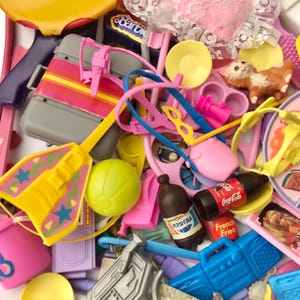 May include: A collection of miniature toys in various colors, including pink, yellow, and blue. Items include a suitcase, a guitar, a ball, a bottle of Pepsi, a bottle of Coca-Cola, and a boombox.