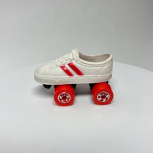 May include: A miniature white roller skate with red stripes and red wheels. The wheels are small and round, and the skate has a classic sneaker design.