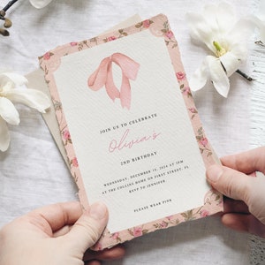 Pu&ograve; includere: Un invito rosa con motivo floreale e un fiocco rosa sul davanti. L'invito recita "Unisciti a noi per celebrare il 2&deg; compleanno di Olivia. Mercoled&igrave; 18 dicembre 2024 alle 15:00 presso la casa dei Collins in First Street, FL. RSVP a Jennifer. Per favore, indossa il rosa."
