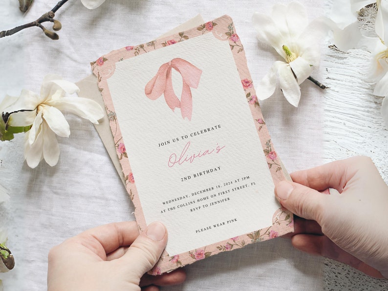 Pu&ograve; includere: Un invito rosa con motivo floreale e un fiocco rosa sul davanti. L'invito recita "Unisciti a noi per celebrare il 2&deg; compleanno di Olivia. Mercoled&igrave; 18 dicembre 2024 alle 15:00 presso la casa dei Collins in First Street, FL. RSVP a Jennifer. Per favore, indossa il rosa."