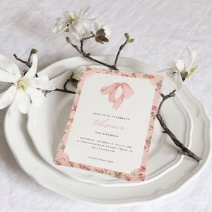 Pu&ograve; includere: Un invito rosa e bianco con motivo floreale e un fiocco rosa in cima. L'invito recita "Join us to celebrate Olivia's 2nd Birthday".