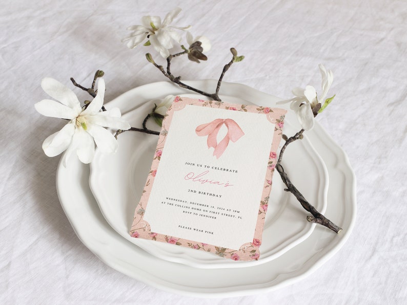 Pu&ograve; includere: Un invito rosa e bianco con motivo floreale e un fiocco rosa in cima. L'invito recita "Join us to celebrate Olivia's 2nd Birthday".