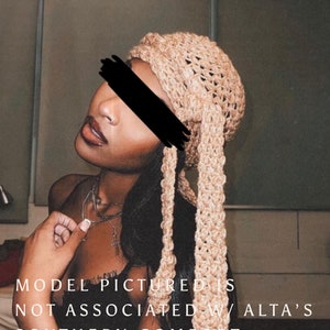 May include: A close-up of a person wearing a light brown crocheted head wrap. The wrap is tied in a knot at the top of the head and the ends are hanging down the back. The person is wearing a black shirt and has dark hair. The text "MODEL PICTURED IS NOT ASSOCIATED W/ ALTA'S SOUTHERN COMFORT" is at the bottom of the image.